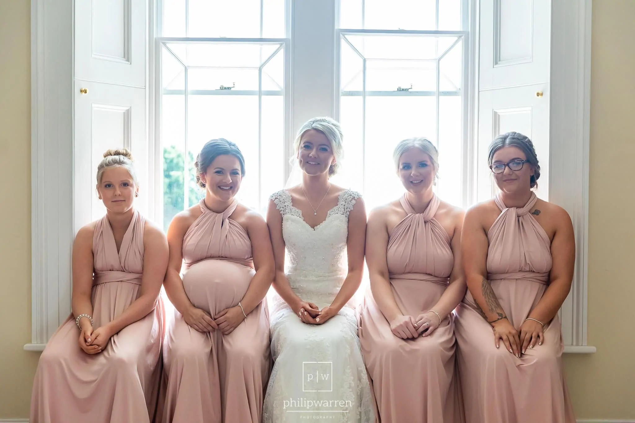 bride and her 4 bridesmaids sitting together in their pink bridesmaids dresses sitting in the window in the south wales wedding venues